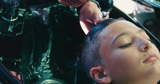 Unrecognizable professional hairdresser washing hair to his client. Barber at work.