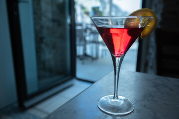 A red drink with a slice of orange in a cocktail glass on a bar table