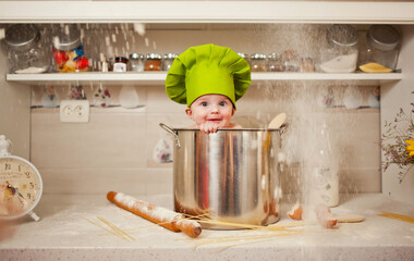 Cute baby chef in a huge pot and flour flows around