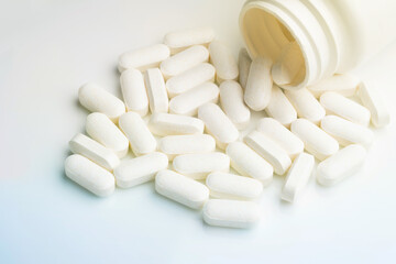 Medication bottle and white pills spilled on white background.