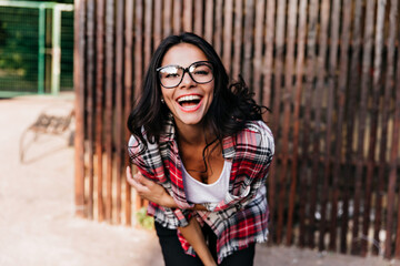 Fototapeta premium Joyful tanned female model has a good time. Brunette inspired lady smiling on wooden background.