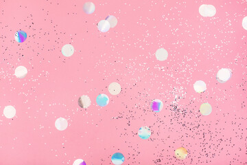 Flying silver holographic confetti on pastel pink background. Festive concept.
