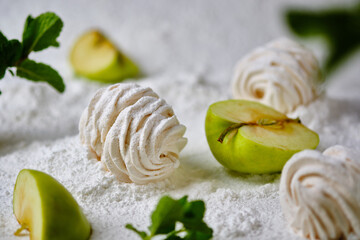 Homemade handmade apple marshmallows on a background of icing sugar. Dessert in the snow. Sweetness is decorated with apples and mint.