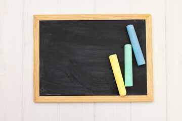 Pieces of chalk on a school blackboard on a white wooden background. Top view. Copy space.