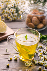 A cup of herbal chamomile tea with camomile blossoms, lemons and mint leaves. The concept of alternative medicine and immune boost