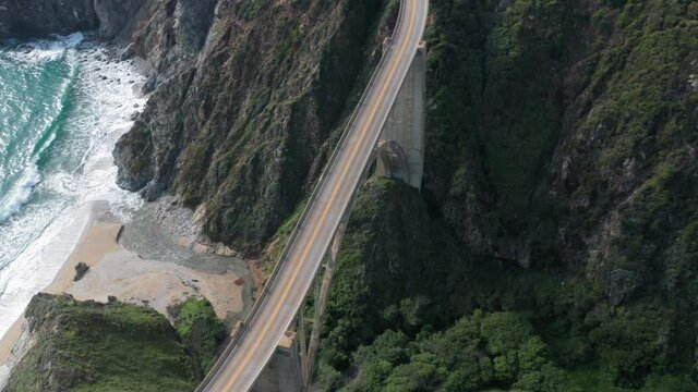 Aerial view of the picturesque arch bridge standing over the canyon among the beautiful hills covered with green grass. Cars move across the bridge. Famous landmark of USA under the cloudy sky. 4K