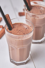 Chocolate milkshake with cinnamon in a glass cup on a white wooden table.