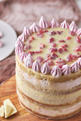 Cake with white chocolate and cherry on a wooden board on a white table. Dessert decorated with homemade marshmallows.