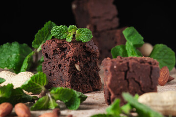Chocolate brownie with nuts and mint. Sweet and tasty dessert decorated with mint, closeup on a wooden table. Soft focus.