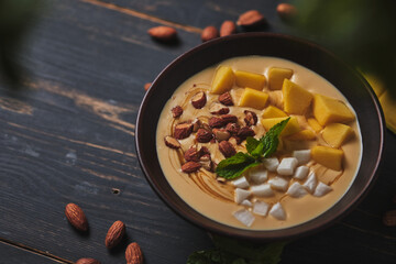 Tropical smoothie bowl with banana, mango, coconut and nuts. Refreshing dessert with mint on an old wooden table. Diet and delicious breakfast for the whole family.