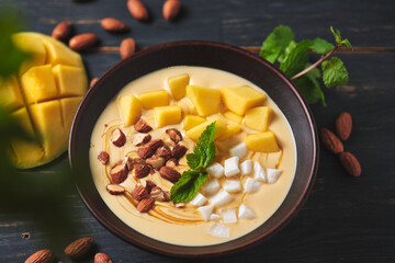 Tropical smoothie bowl with banana, mango, coconut and nuts. Refreshing dessert with mint on an old wooden table. Diet and delicious breakfast for the whole family.