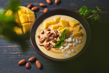 Tropical smoothie bowl with banana, mango, coconut and nuts. Refreshing dessert with mint on an old wooden table. Diet and delicious breakfast for the whole family.