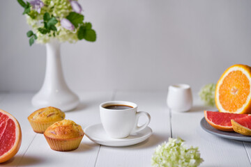 Coffee and fruit muffins with fresh peach for breakfast. Morning table with dessert, espresso, fruits and flowers in a vase on a white wooden table.