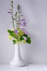 Flowers in a vase on a white wooden table. Morning, rustic still life.