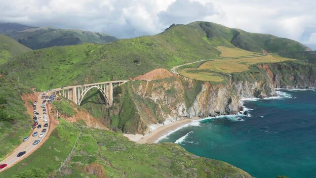Breathtaking distant view over the famous beautiful landmark, Bixby Bridge. The arch bridge on the Big Sur coast of California. Lots of cars are seen on the view point and on the way to the bridge. 4k