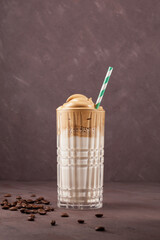 Korean drink Dalgona coffee in glass. Cold milk with foam of instant coffee on brown background. Vertical shot