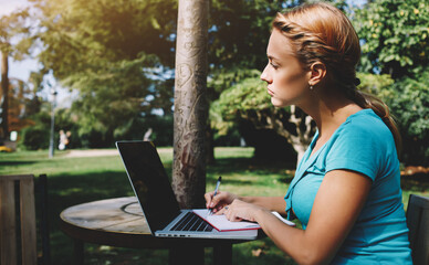 Gorgeous young woman is reading interesting book during her recreation time in summer weekend,