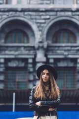 Attractive female standing with crossed arms on the street, glamorous hipster girl looking at you
