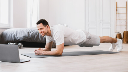 Man Exercising At Laptop Doing Plank During Online Workout Indoors