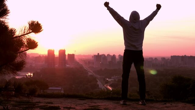 silhouette man in casual hoodie raising hands celebrate success looking on the cityscape at sunrise urban city view in the morning