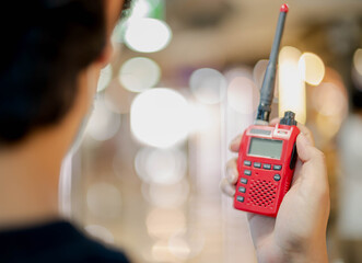 The male hand holding with a red Walkie Talkie or Portable radio transceiver for communication. © siewwy84