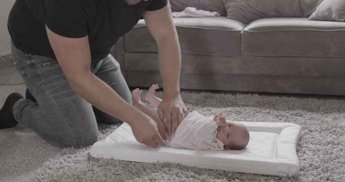Father kneeling on floor, changing nappy of his newborn baby girl.