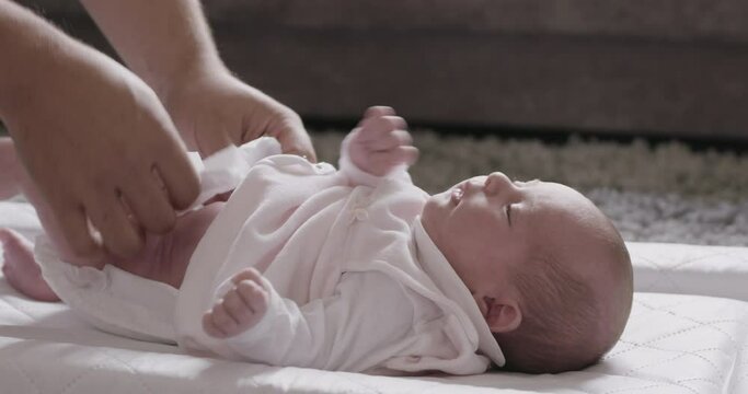 Father kneeling on floor, changing nappy of his newborn baby girl.