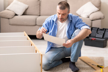 Man Assembling Cabinet Sitting Reading Installation Instruction At Home