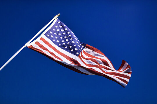 American Flag on the flagpole is waving in the wind against a blue sky.