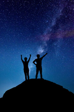 Milky Way with people on the mountain. Landscape with night sky with stars and silhouette of standing happy man and woman who pointing finger in starry sky. Milky way with travelers. Beautiful galaxy