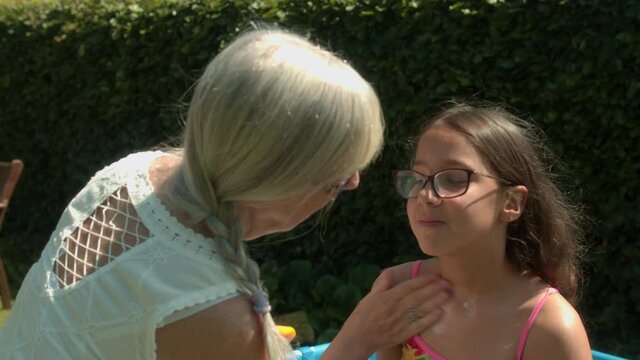 Grandmother Applying Suntan Lotion Onto Her Granddaughter's Body. 