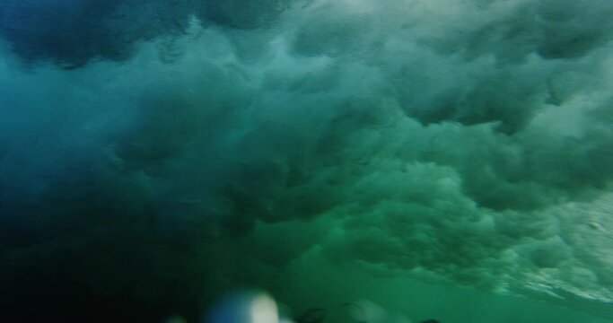 A large wave breaking into an arc into a dark blue sea with large plumes of spray, view ending up under the water.