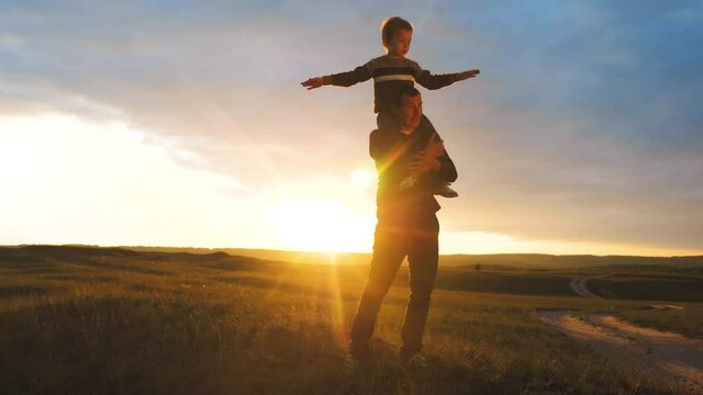 happy family. son sits on his neck teamwork at father shows hands to the side plays at the pilot depicts an airplane silhouette at sunset. happy family concept childhood man dad with little lifestyle