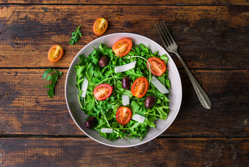 Salad bowl with arugula rocket salad, black olives, cherry tomatoes, and hard cheese. Concept of healthy, vegetarian and vegan food