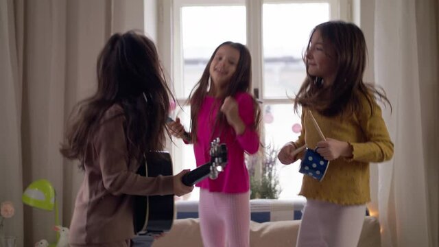 Group of small girls friends playing guitar and jumping on slumber party.
