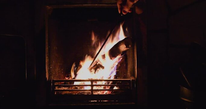 A person using a poker to prod teh fire in a grate, a log burning well. 