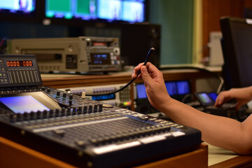 Closeup of sound engineer's hand moving sliders on audio mixing board.