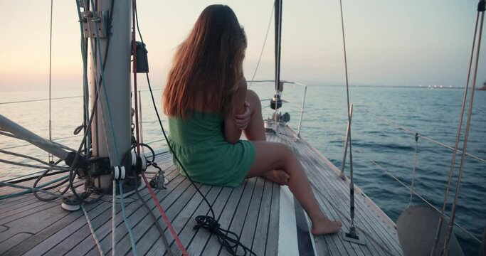 Young woman wearing green sundress enjoying trip on a sailboat in the Ligurian Sea, taking pictures with her mobile phone.