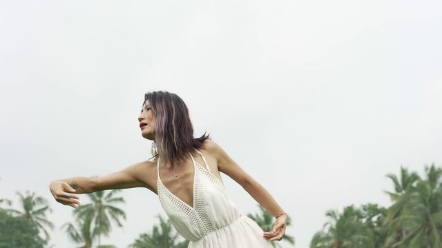 mind and body connection with nature - middle aged attractive and happy Asian Chinese woman in Summer dress enjoying dancing free at idyllic tropical green field
