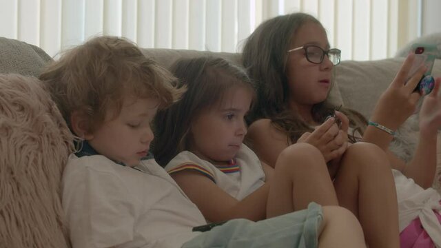 Boy and two girls sitting on sofa in living room, using mobile phone.