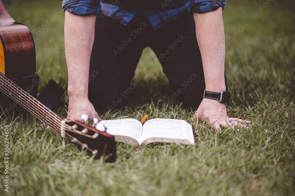 Poster man with a guitar and an open book on the grass