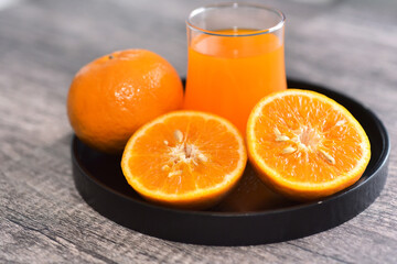 orange cut in half with the glass of orange juice on black tray