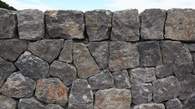 Close up of the top of a grey dry stone wall, blue sky above.