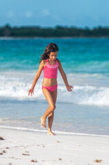 Fototapeta na wymiar Niña en bikini rosa camina por playa azul del mar Caribe en vacaciones de verano.