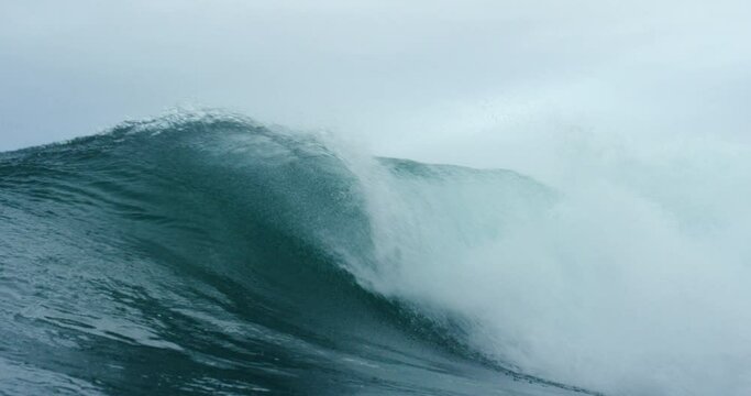 A large wave breaking into an arc into a dark blue sea with large plumes of spray.