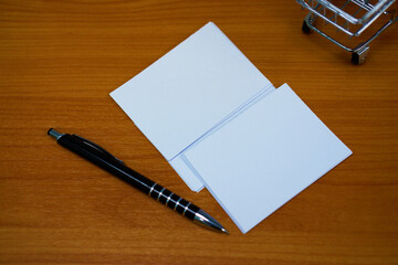 Stacked paper of blank white business cards simulated with an elegant black pen on the wooden table background.