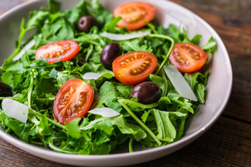 Salad bowl with arugula rocket salad, black olives, cherry tomatoes, and hard cheese. Concept of healthy, vegetarian and vegan food