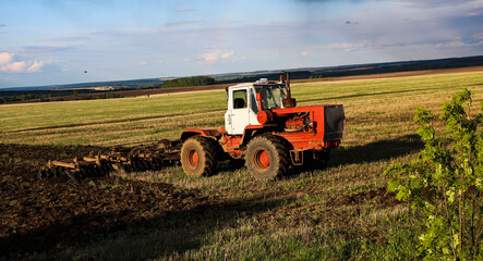 Obraz premium tractor plows and harrows land in large field on sunny spring day. preparing soil for planting crops, plowing soil with tractor with disk plow.