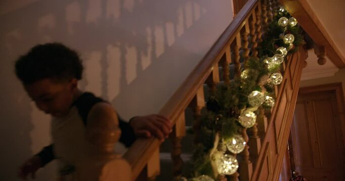 MS HANDHELD Boy (6-7) Wearing Pajamas Running Down Stairs Decorated With Christmas Garland At Night / Dinton, Wiltshire, UK