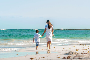 Fototapeta na wymiar Mujer y niño con ropa de verano pasea juntos en playa del mar Caribe durante las vacaciones.